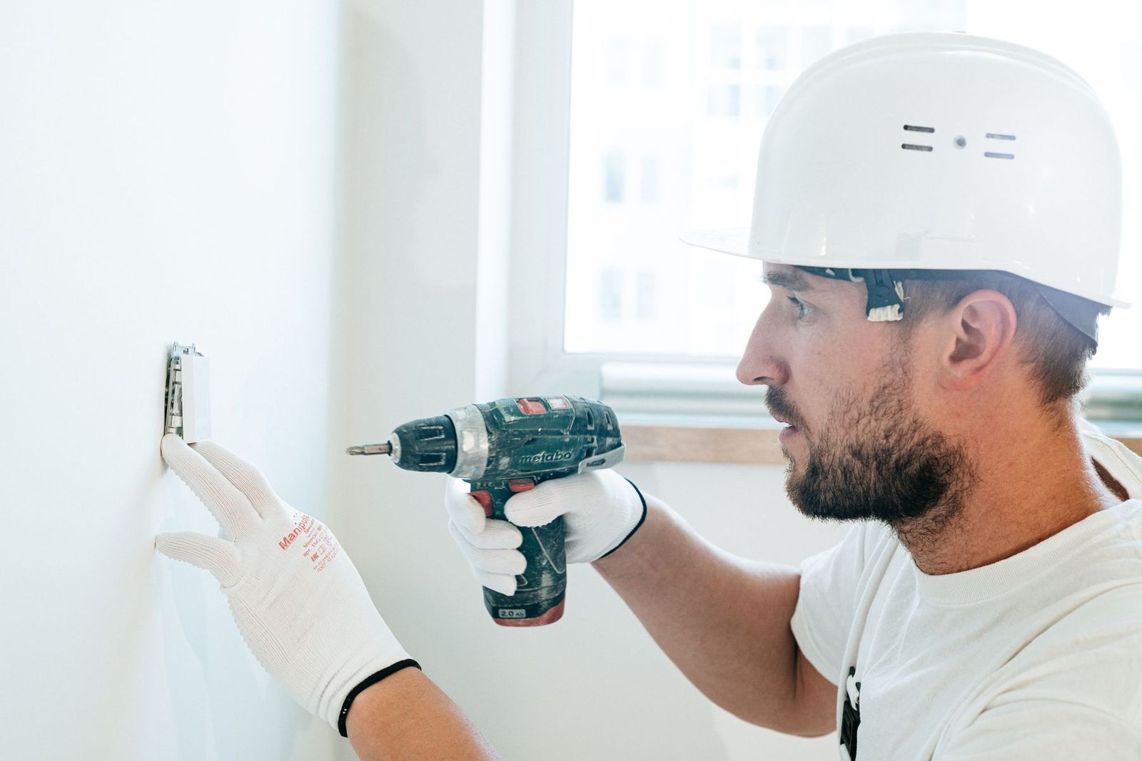 Handwerker mit Schutzausrüstung bohrt in eine Wand